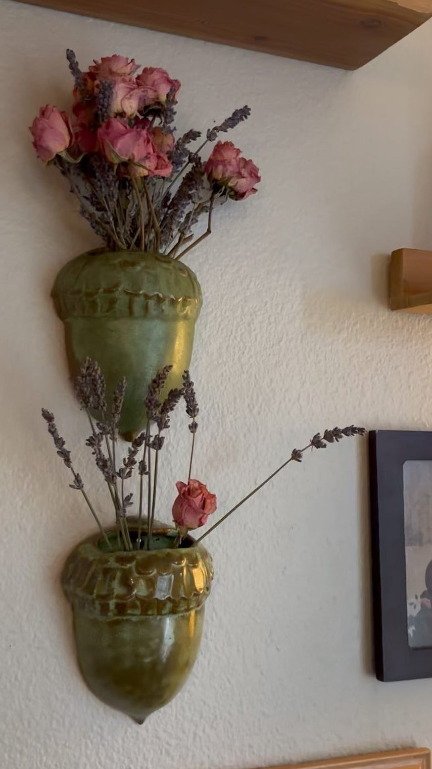 Decorative wall art with green vases and dried flowers on a white wall.